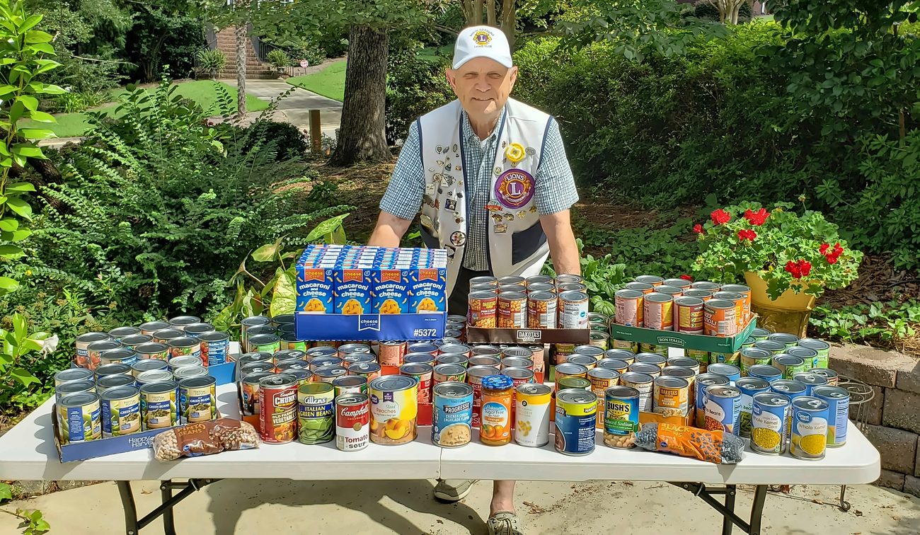 A Lexington Lions Club member standing behind a table piled with canned food donations.