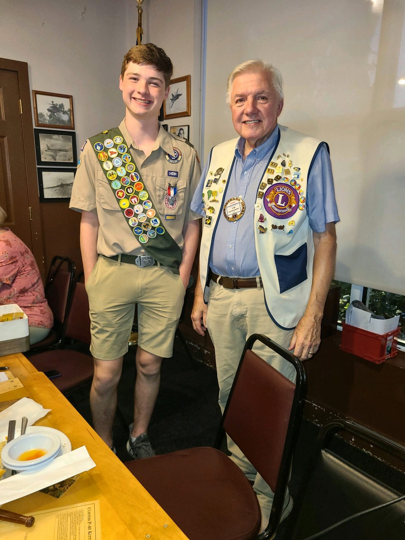 A Boy Scout wearing a merit badge sash standing with a Lexington Lions Club member.